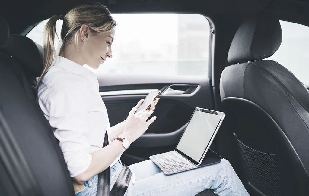 Female entrepreneur using mobile devices while at airport limousine passenger seat